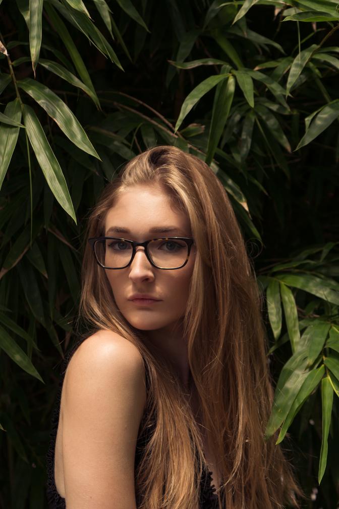 A woman looking over her shoulder at the camera, in front of a wall of ferns